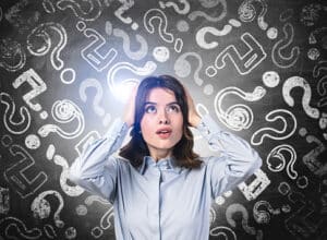 Thoughtful businesswoman wearing shirt is holding head with her hands. Sketch with lots of question marks on chalkboard in the background. Concept of searching for solution to buying life insurance.