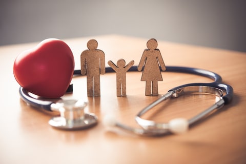 Wooden familty standing next to wooden red heart with a stethoscope wrapped around them on a tabletop representing health insurance for self employed Oklahoma Sung Kang Insurance Agency